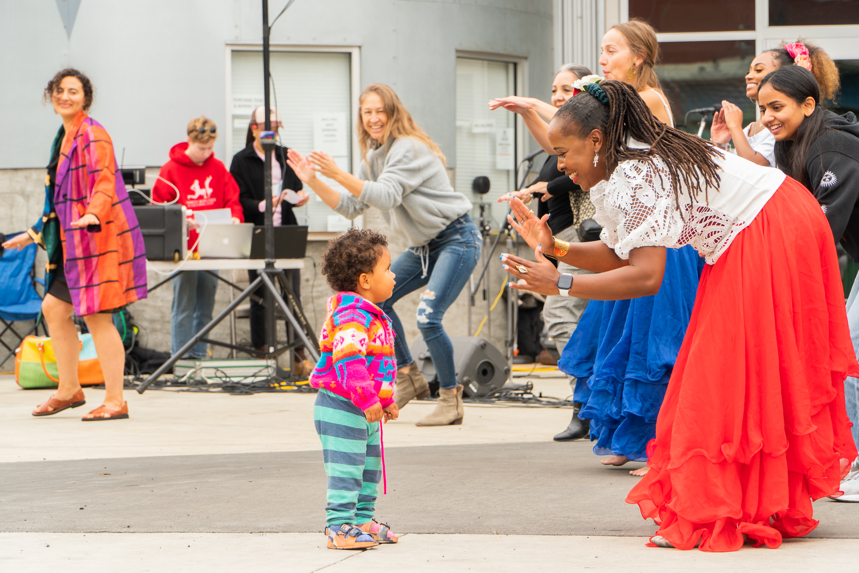 Dandha Da Hora leads a dance with a child and community members at an outdoor festival.