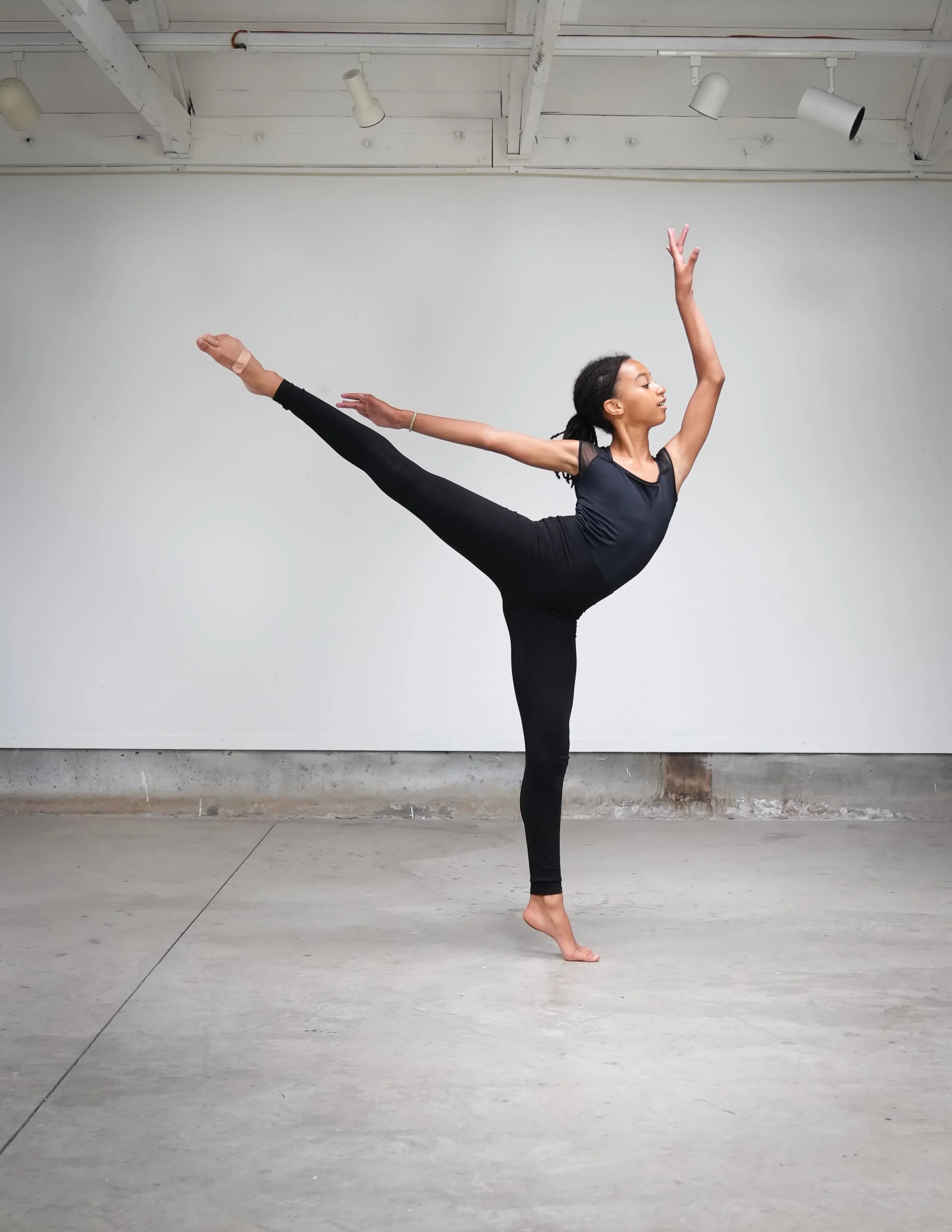 Dancer in a high side kick, arms reaching overhead.