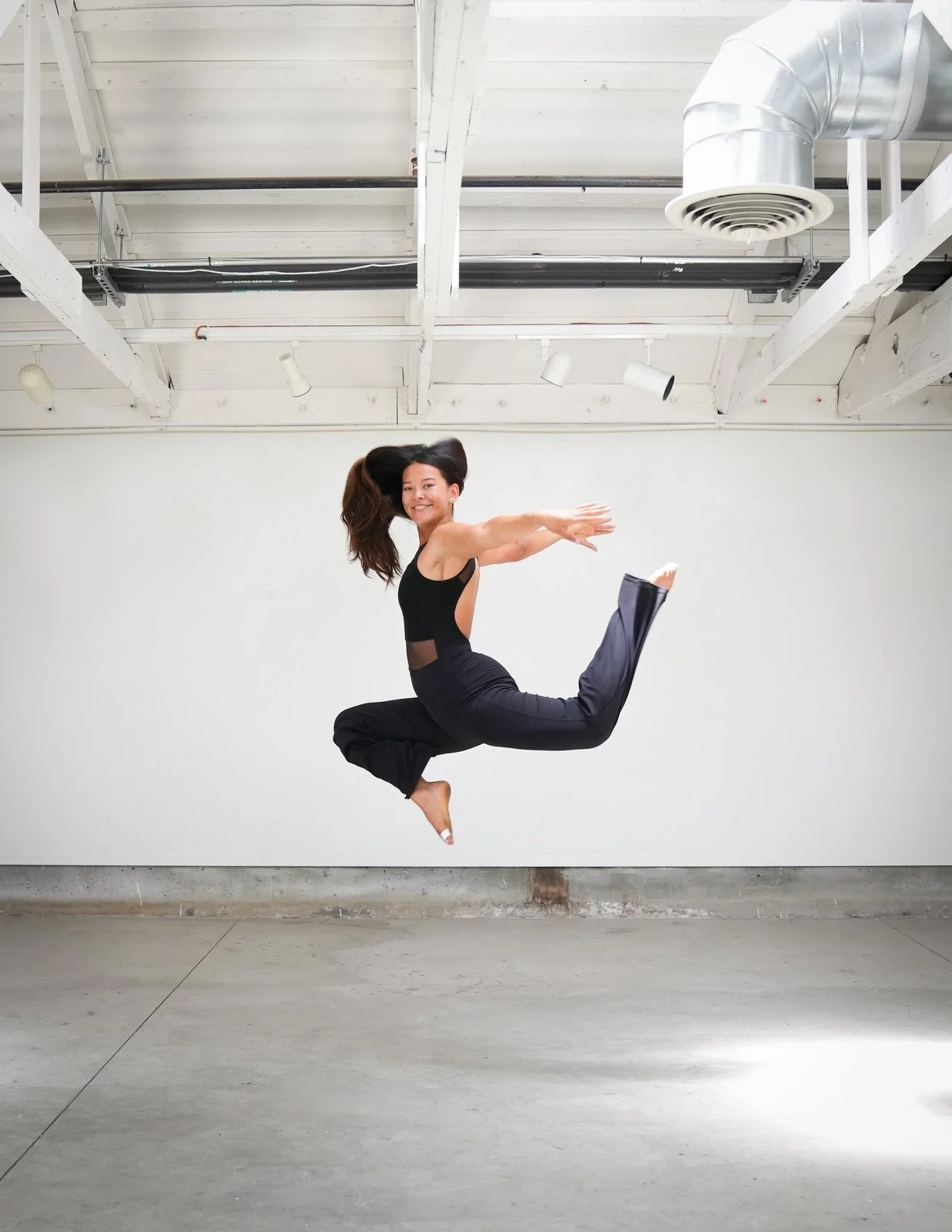 Dancer leaping mid-air, ponytail flying, smiling.