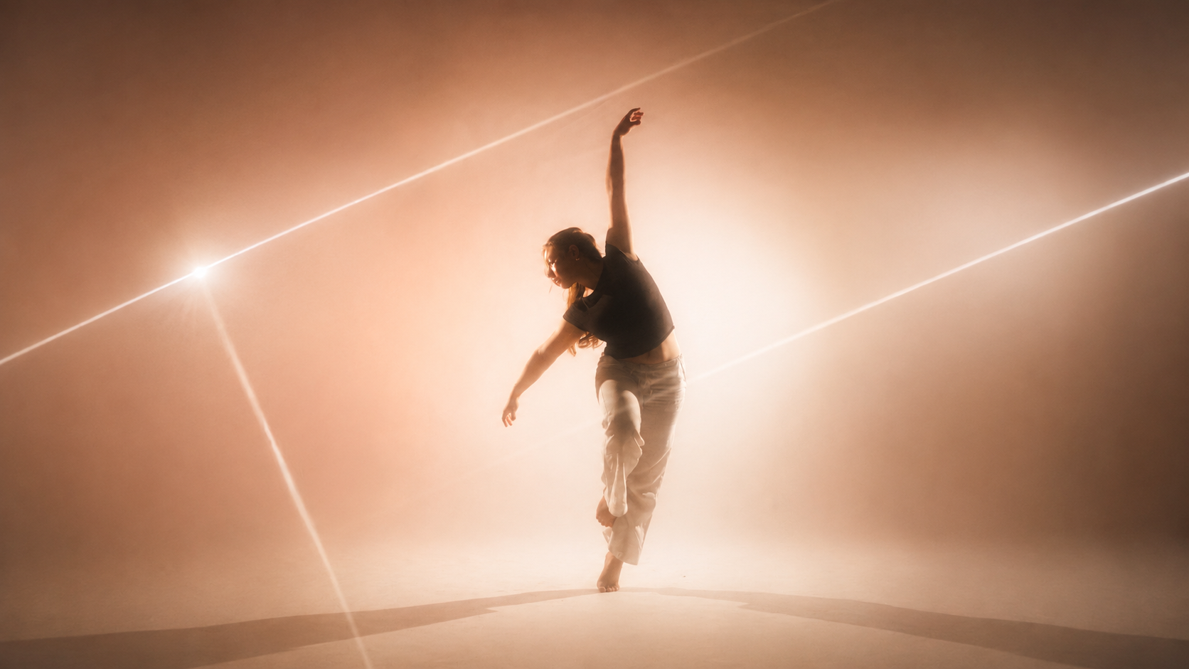 A dancer silhouetted in warm, hazy light, one leg lifted mid-movement.
