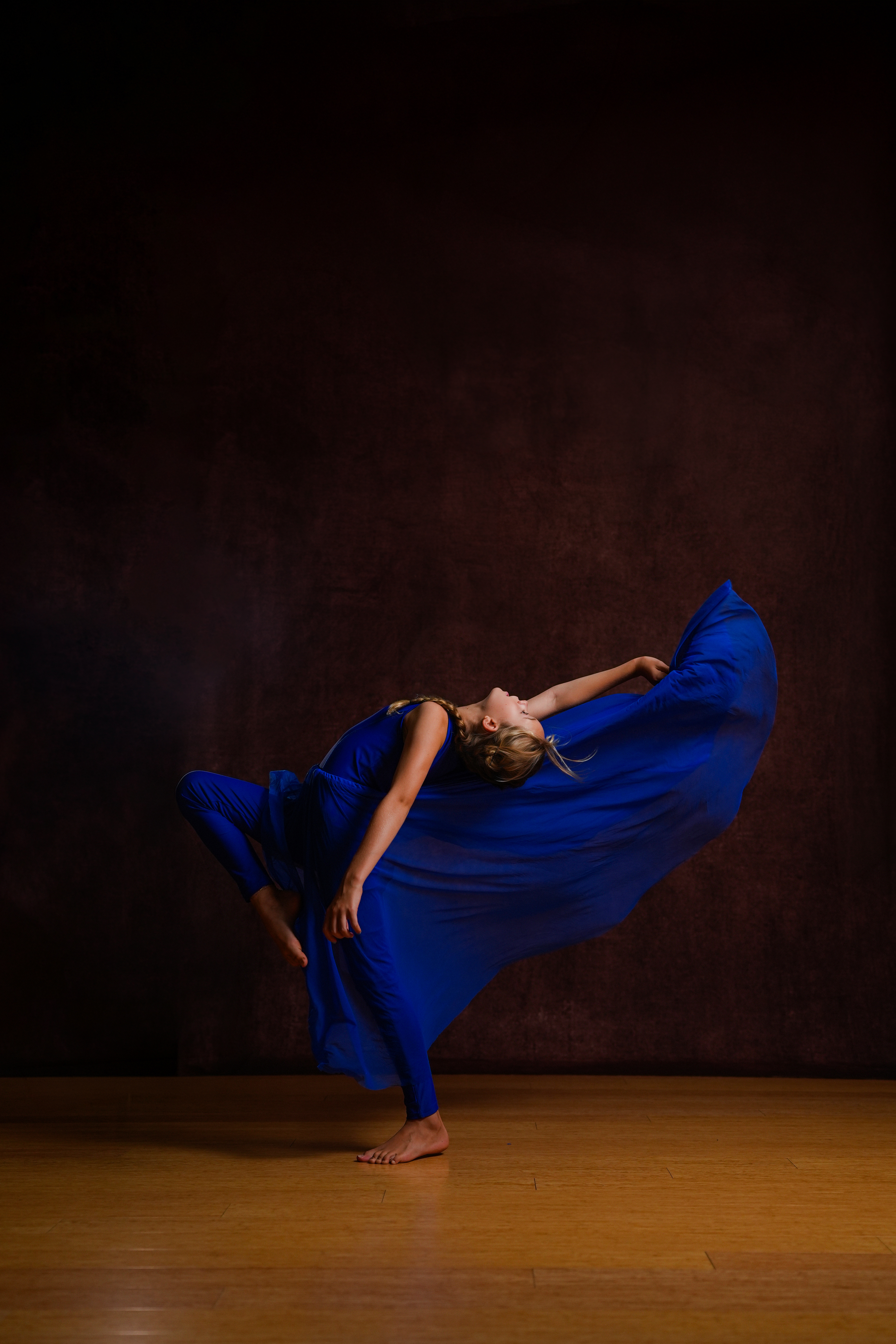 A dancer in a vivid blue costume performs a supported dance pose on stage.